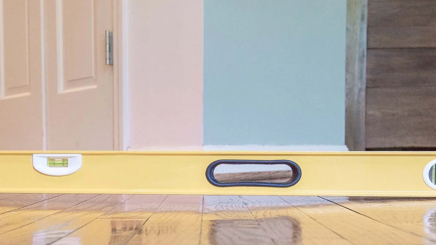 Yellow spirit level on polished wooden floor highlighting sloping floor issues and foundation settling, showcasing expert inspection by Golden Bay Foundation Builders.